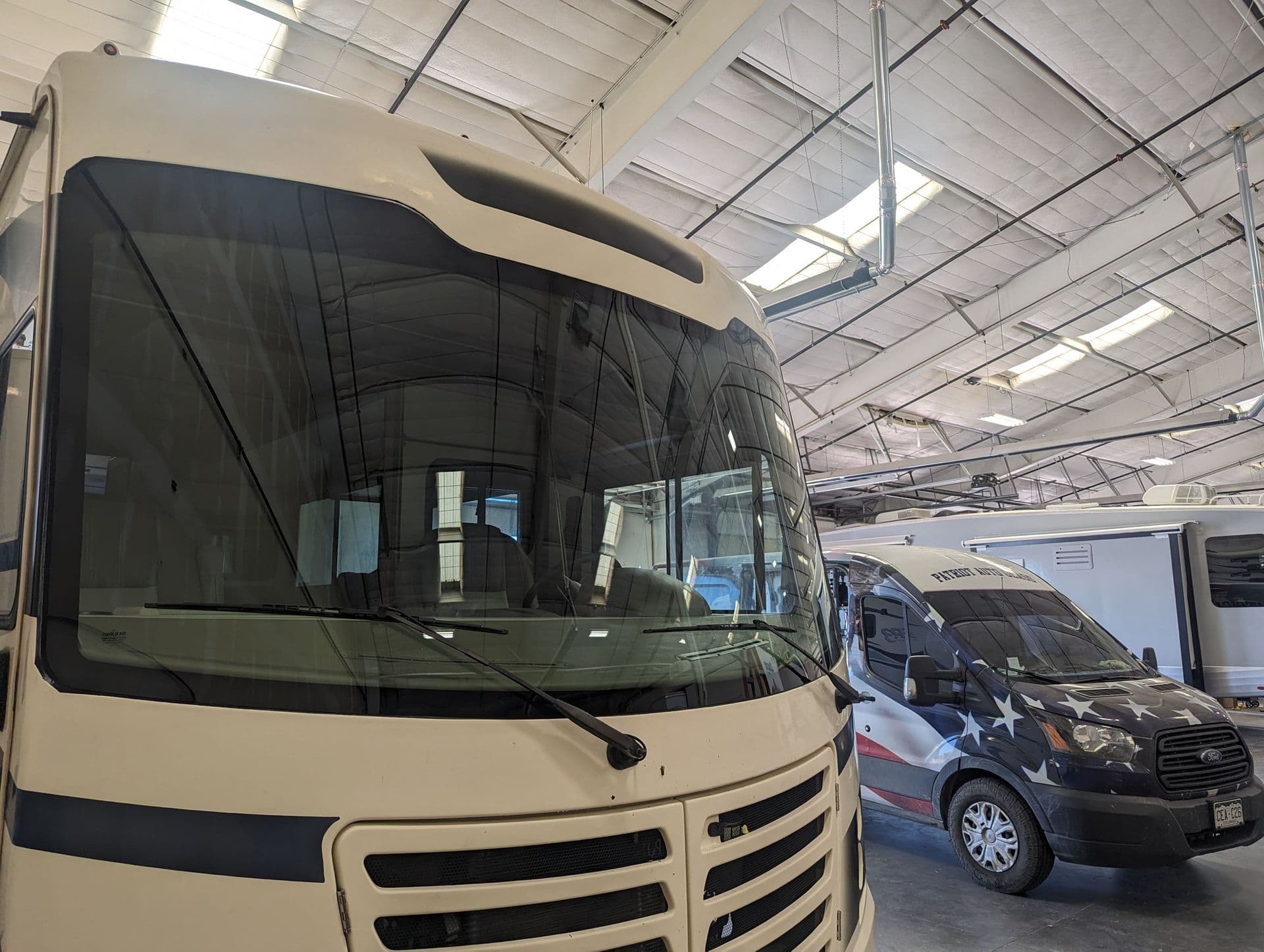 Class A motorhome windshield in the shop beside the Patriot Auto Glass service van